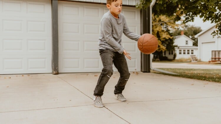 Young boy playing with a basketball in driveway if home